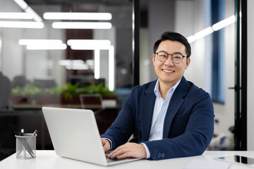 Portrait of successful mature asian businessman, experienced boss in business suit smiling and...