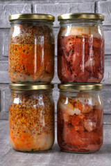Different canned stewed meat in glass jars on the table against the gray background. Canned pork and buckwheat, ready-made meal