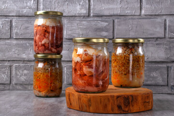 Different canned stewed meat in glass jars on the table against the gray background. Canned pork...