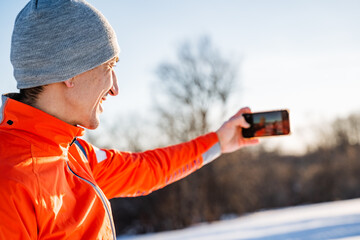 Man taking selfie on phone while standing in winter forest, guy taking pictures of himself on...