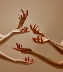 Graceful hands streaming upwards illuminated warm light against beige background in studio. Concept of art, human touch, femininity, beauty and care, spa procedures, treatments.