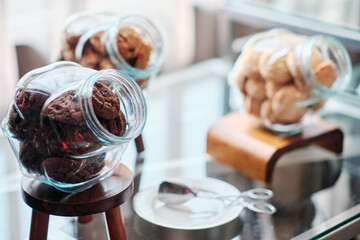 dark chocolate cookies in a jar and other two jars full with milk cookies stay on the table serving...