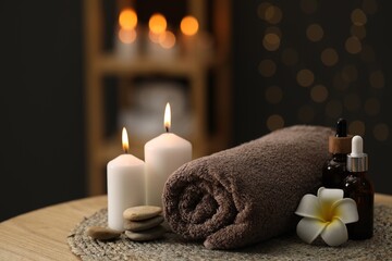 Fototapeta na wymiar Spa composition. Rolled towel, cosmetic products, stones, burning candles and plumeria flower on table indoors, closeup. Space for text