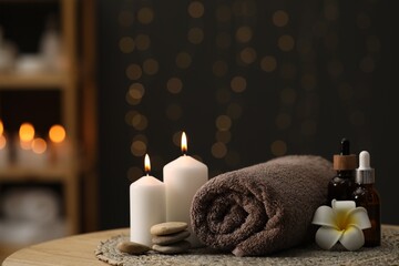 Spa composition. Rolled towel, cosmetic products, stones, burning candles and plumeria flower on table indoors. Space for text
