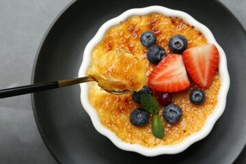 Taking delicious creme brulee with berries and mint from bowl at grey table, top view