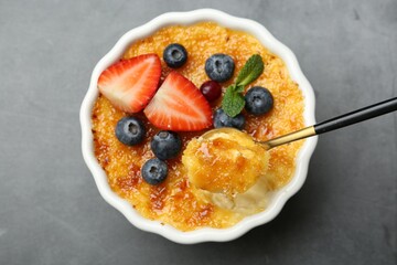 Taking delicious creme brulee with berries and mint from bowl at grey table, top view