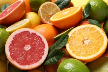 Different fresh citrus fruits and leaves as background, closeup