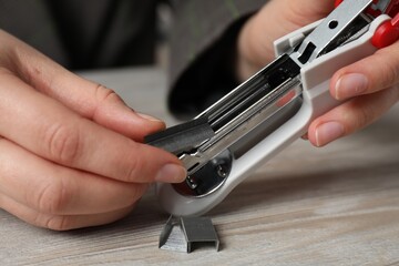 Woman putting metal staples into stapler at wooden table, closeup
