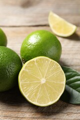 Whole and cut fresh limes on wooden table, closeup