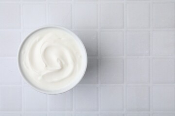 Delicious natural yogurt in bowl on white tiled table, top view. Space for text