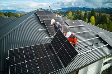 Tapeten Roofers building photovoltaic solar module station on roof of house. Men electricians in helmets installing solar panel system outdoors. Concept of alternative and renewable energy. Aerial view. © anatoliy_gleb