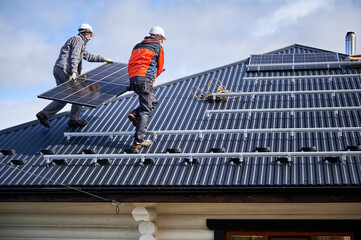 Roofers building solar panel system on roof of house. Men workers in helmets carrying photovoltaic...