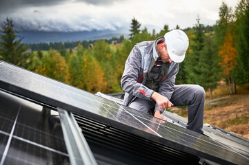 Man mounter mounting photovoltaic solar panels on roof of house. Engineer in helmet installing...