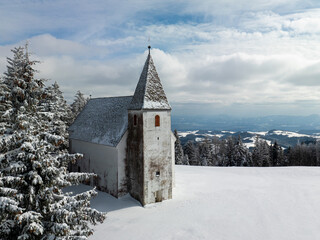 Fototapeta na wymiar Church on top of the hill in winter next to ski resort. With beautiful landscape view on cloudy day