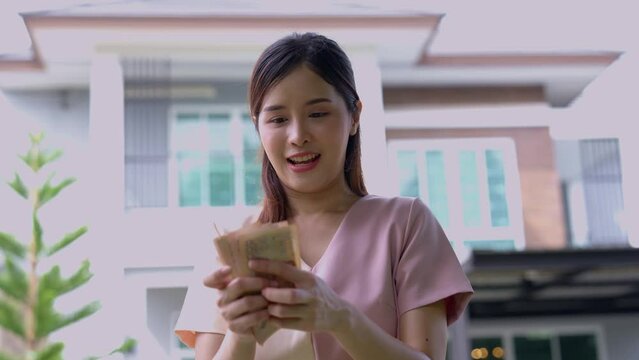 Portrait of happy attractive Asian women holding a lot of banknotes in front of home to celebrate and Pay the final installment of the house, Loans for real estate concept, Smiling young successful
