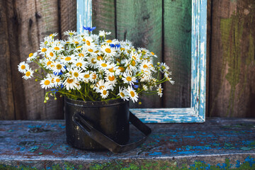 A bouquet of daisies and cornflowers in a decorative old pot against the background of an old wooden wall, close-up. Summer bouquet of meadow herbs