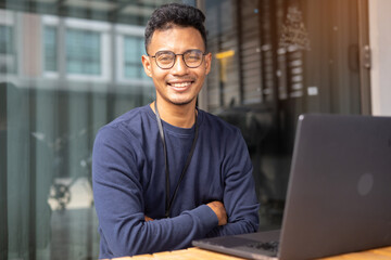 Fototapeta premium close up adult indian programmer man arm crossed while looking with confident smile at indoor office workplace for business startup and technology concept