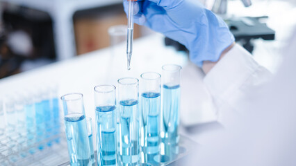 Close-up hands dropping fluid from dropper flask beaker into blue test tube sample laboratory for compare in medicine chemical biology medical science experiment technology biotechnology analysis