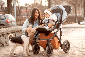 Happy Caucasian young woman walking in the park with her one-year-old daughter in buggy.The child...