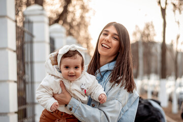 Obraz premium A young happy dark-haired woman carries her one-year-old daughter in her arms while walking.A family concept.Happy motherhood.
