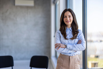 Successful businesswoman standing in creative office and looking at camera. Young woman entrepreneur in a coworking space smiling. Por of business team at modern agency with copy space.