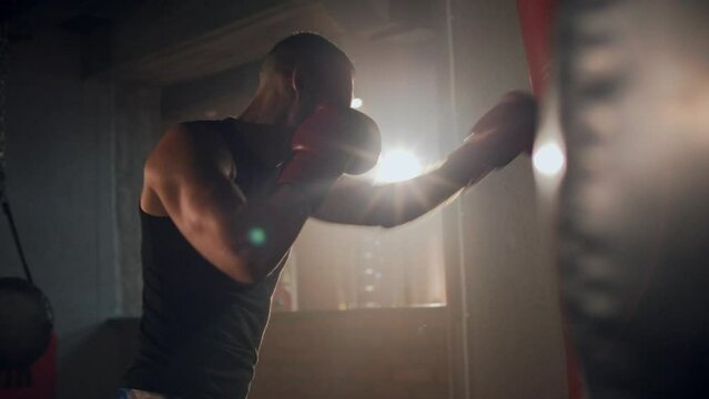 Sport motivation, medium shot of athlete man boxing in the old school gym. Fit strong man training with boxing bag