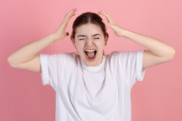 Angry attractive caucasian young brunette woman in casual white t-shirt with eyes closed yells...