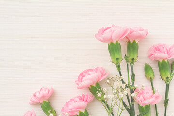 Pretty frame of pink carnations and white hazel with copy space on white wood grain background