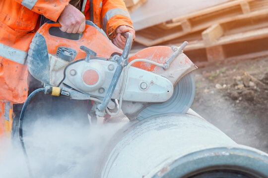 Construction worker cutting concrete pipe for drainage using a cut-off saw. Cutting concrete with a diamond blade creating cloud of silica dust