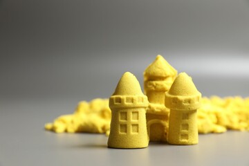 Castle figures made of yellow kinetic sand on grey background, closeup. Space for text