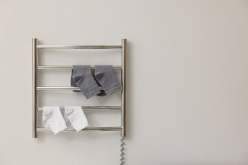 Heated towel rail with socks on white wall, space for text