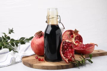 Foto auf Leinwand Tasty pomegranate sauce in bottle, branches and fruits on light table, closeup © New Africa