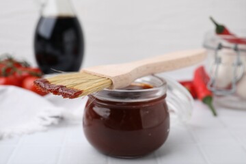 Marinade in jar and basting brush on white table, closeup