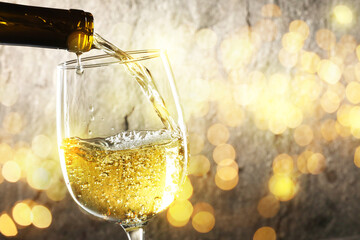 Pouring white wine into glass against background with blurred lights, closeup. Space for text
