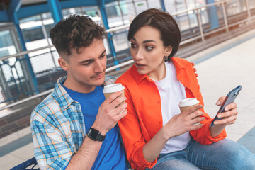 a young couple traveling together, waiting for a bus with luggage, drinking coffee, using phone  Traveling together concept