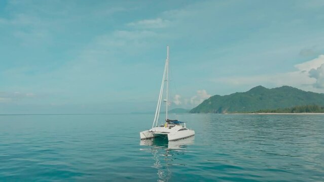 A catamaran is anchored in a calm sea near the shoreline