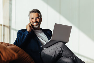 Cheerful businessman with laptop and phone in modern office setting with sunlight
