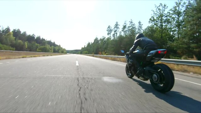 Aerial shot of man riding fast on modern sport motorbike at highway during summer day. Motorcyclist racing his motorcycle on country road. Guy drive bike during trip. Concept of freedom and adventure