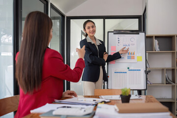 Two businesswomen discussing project strategy in office conference room Businesswoman discusses project planning with colleagues in modern workplace, gives advice on financial data report