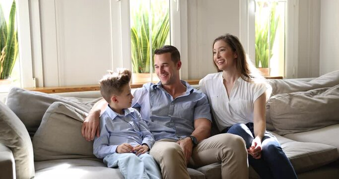 Family with little son enjoy pleasant talk relax together on sofa in cozy sunny living room at own or rented apartment, having joyful conversation, share thoughts, joking, planning weekend feel happy