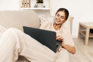 Smiling woman working on laptop in cozy living room, surrounded by modern technology and comfortable lifestyle.