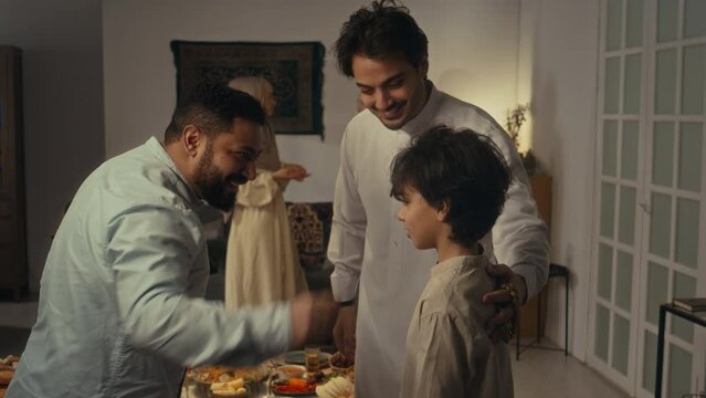 Side footage of cheerful islamic male relatives in kurtas hugging while greeting each other and reuniting to celebrate Eid al-Fitr or Uraza Bayram at home