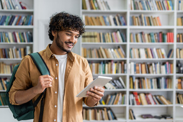 A cheerful young adult holding a digital tablet and carrying a backpack, standing in front of a bookshelf in a well-lit library. The image exudes a vibe of education, technology, learning.
