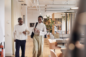 Happy male and female business professionals walking in office corridor