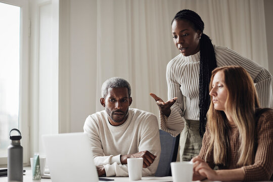 Businesswoman explaining colleagues while looking at laptop in office