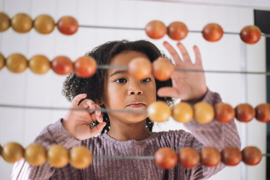 Girl with curly hair learning to count using abacus in classroom at kindergarten