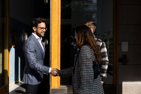 Male real estate agent doing handshake with clients in front of apartment