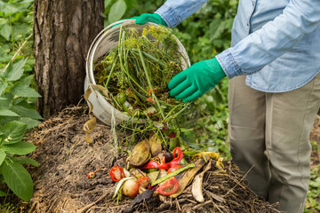 Compost heap pile with bio waste. Farmer gardener hands put vegetable fruit scraps and grass from...
