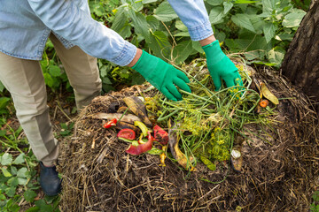 Compost heap pile with bio waste. Farmer gardener hands put weeds grass plants, vegetable fruit...