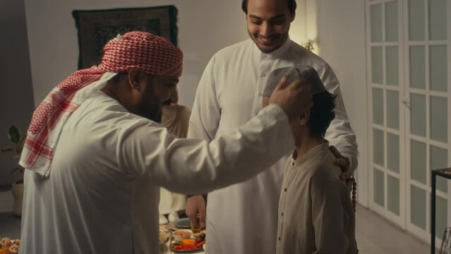 Side footage of positive Biracial bearded man in traditional clothes greeting his Arab brother and nephew at home gathering together to celebrate islamic holiday Uraza Bayram